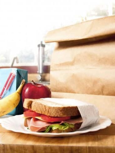 A ham sandwich with apple, banana, and juice carton on a table.