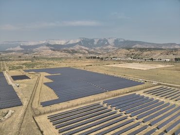 A drone photo of a solar array in the forground with distant mountains  in a smoky haze