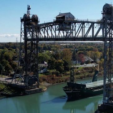 A cargo ship passing under a tall steel lift bridge over a river.