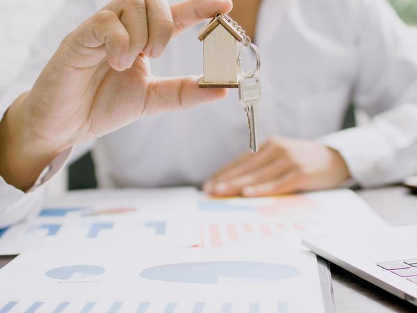 Person holding a house-shaped keychain with a key, symbolizing real estate or home ownership.