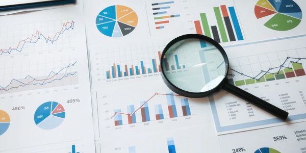 Magnifying glass over various colorful charts and graphs on paper.