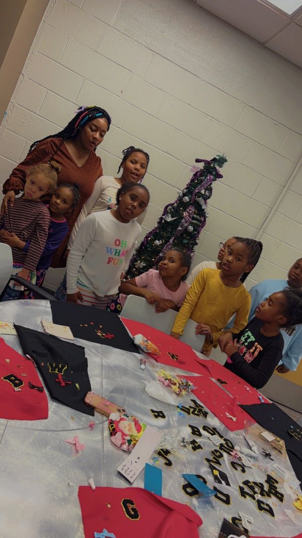 A group of children and a woman gathered around a table with craft supplies near a decorated Christmas tree.