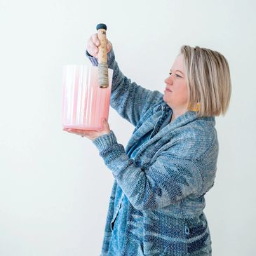 Woman holding a pink planter and wooden tool carefully.