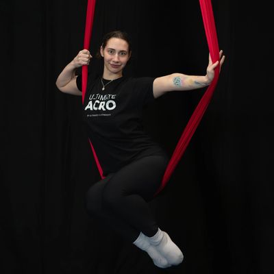 Woman performing aerial acrobatics on red silk ropes against a black background.
