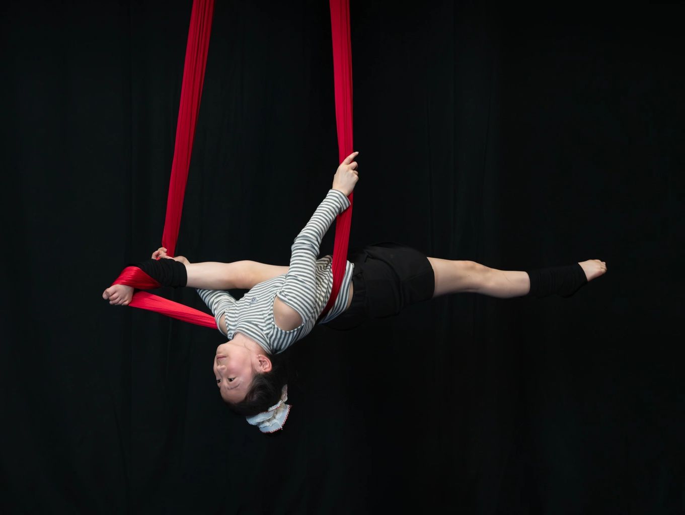 Young girl performing aerial silk acrobatics against a black backdrop.