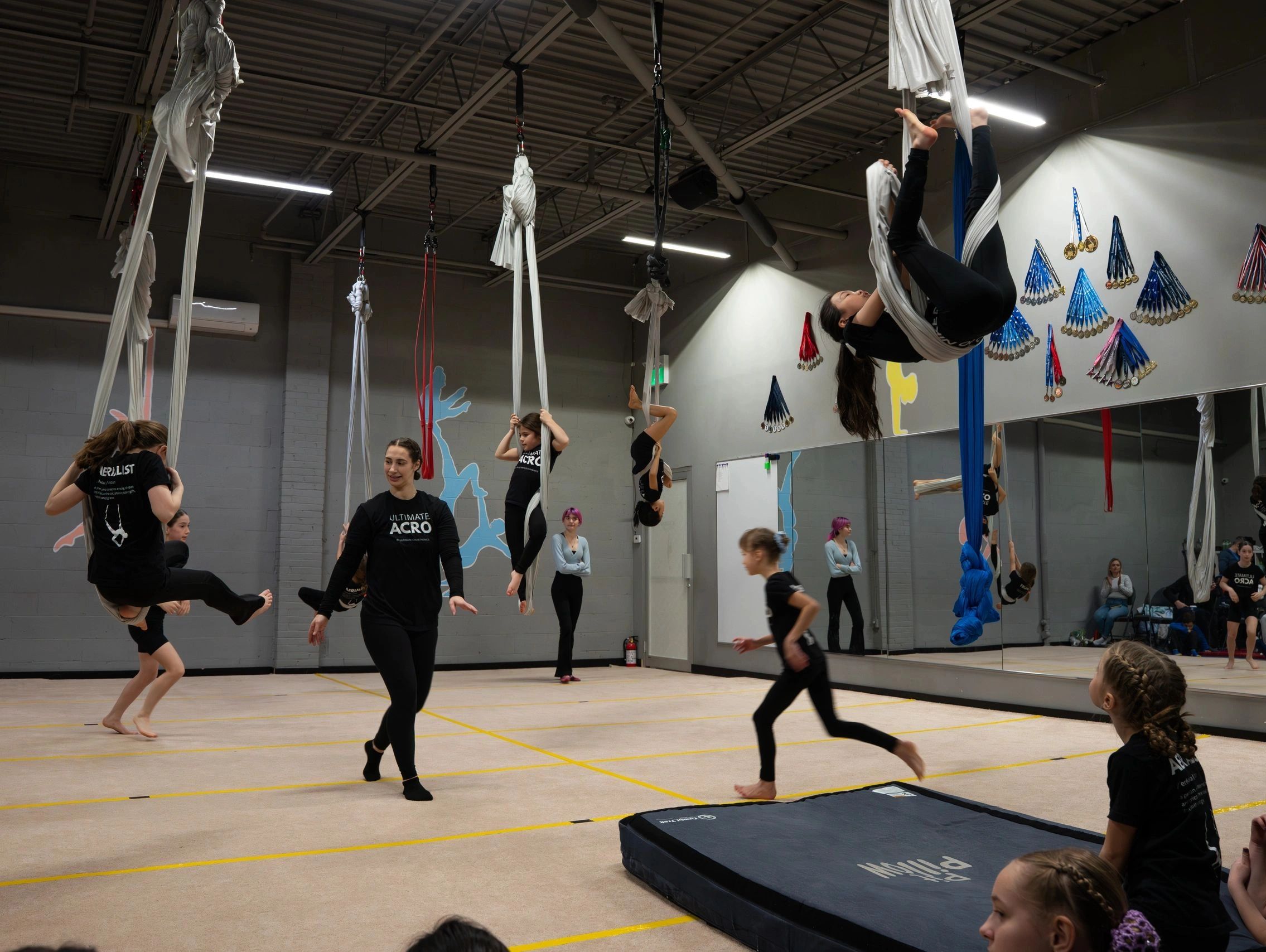 Children practicing aerial silks in a gym with an instructor.