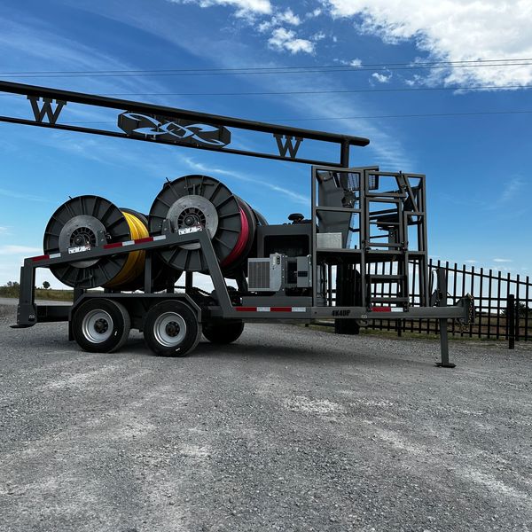 Trailer with large cable reels and equipment under a blue sky.