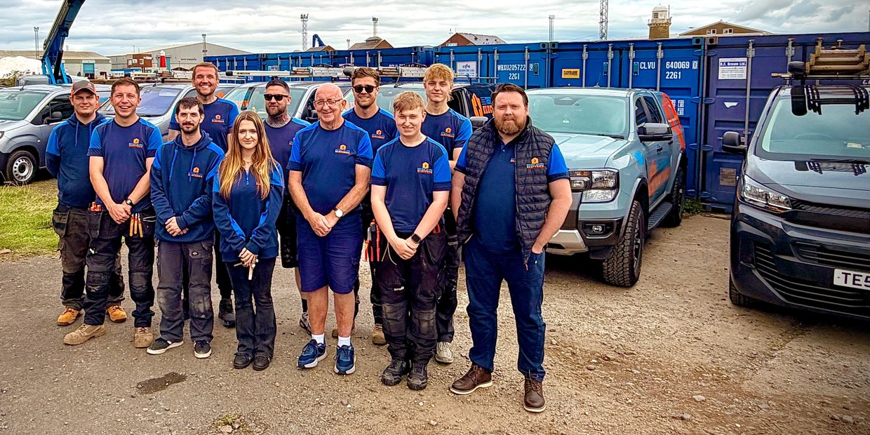 A team of workers posing in front of vehicles and containers.