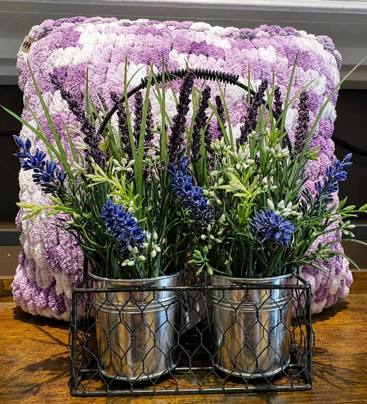 Metal buckets with artificial flowers in front of a fluffy purple and white pillow.