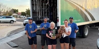 Five movers and a woman holding a dog posing in front of a moving truck.
