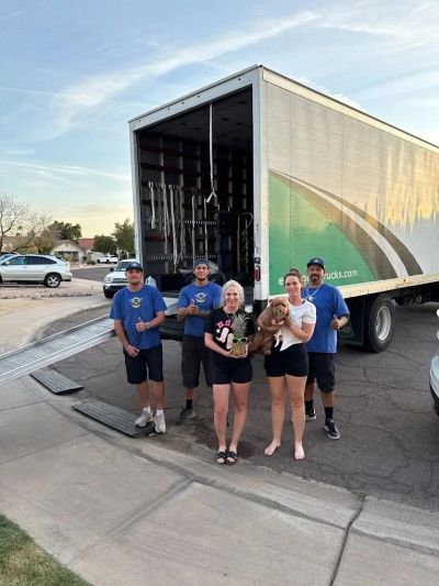 A moving crew with happy customers holding a dog in front of a moving truck.