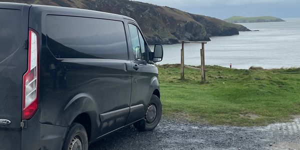 Black van parked near a coastal cliff with cloudy sky.
