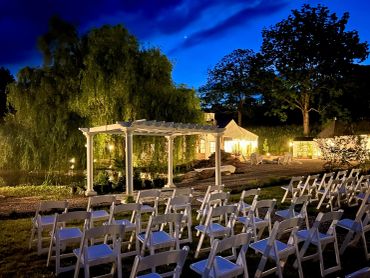 Outdoor wedding setup with chairs and pergola at dusk.