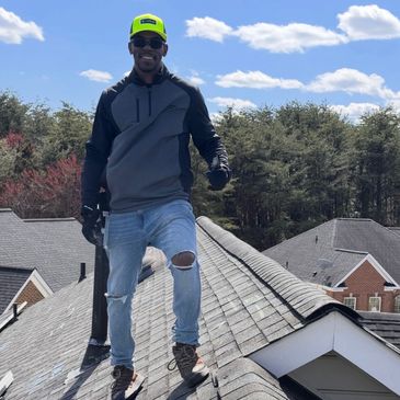 Man in a neon cap and ripped jeans stands confidently on a rooftop under a blue sky.