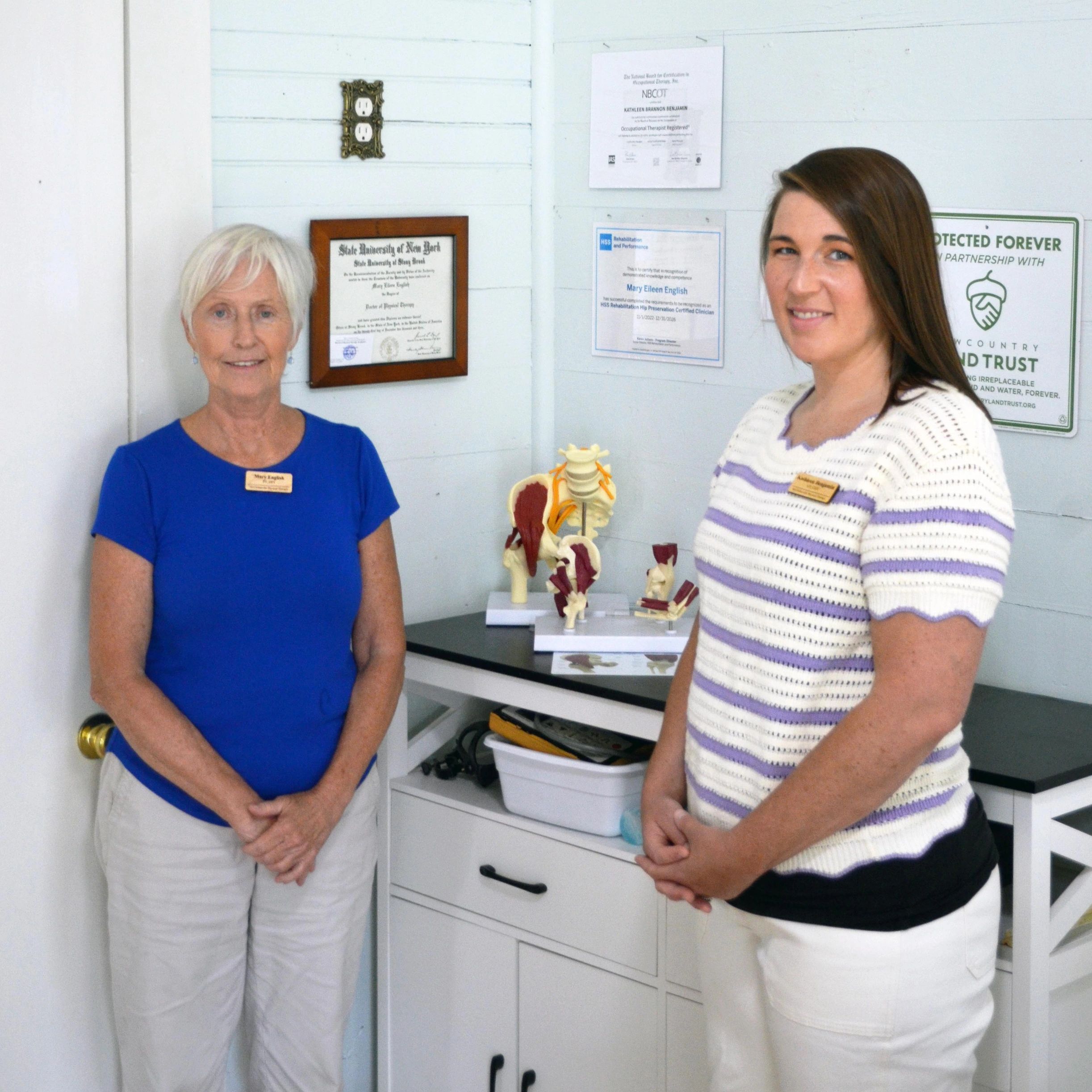 Two women standing in an office with certificates on the wall.