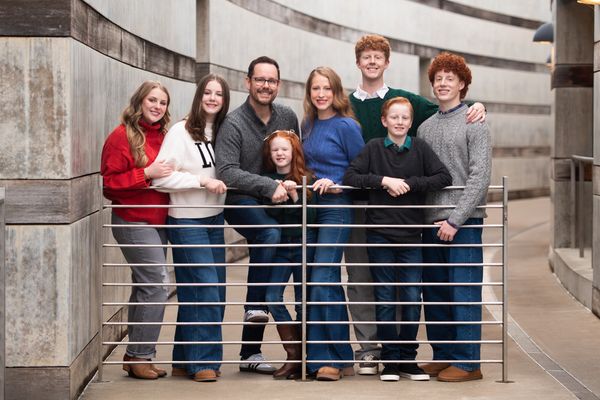 Family of eight posing by a railing outdoors.