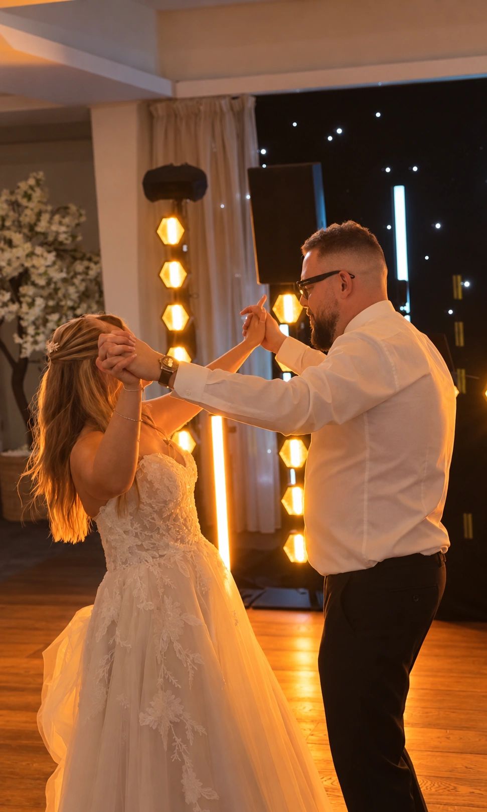 A couple dancing at a wedding reception with warm lighting.