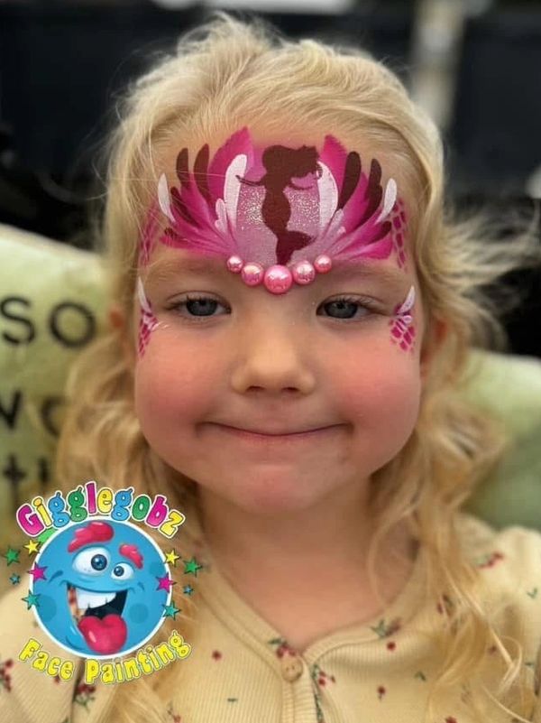 Young girl with colorful face painting featuring a silhouette and decorative pink pearls.