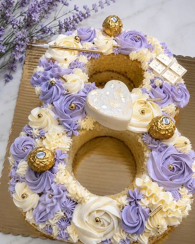 Number 8 cake decorated with purple and white frosting, chocolates, and a heart-shaped topper.