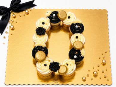 Elegant black and gold themed cupcakes arranged in a zero shape on a golden board.