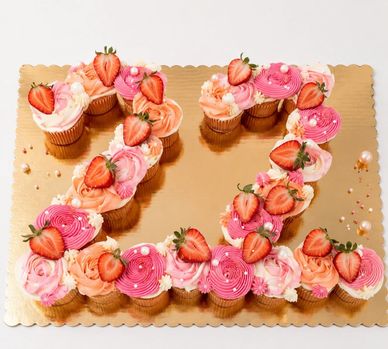 Cupcakes decorated with pink frosting and strawberries shaped as the number 22.
