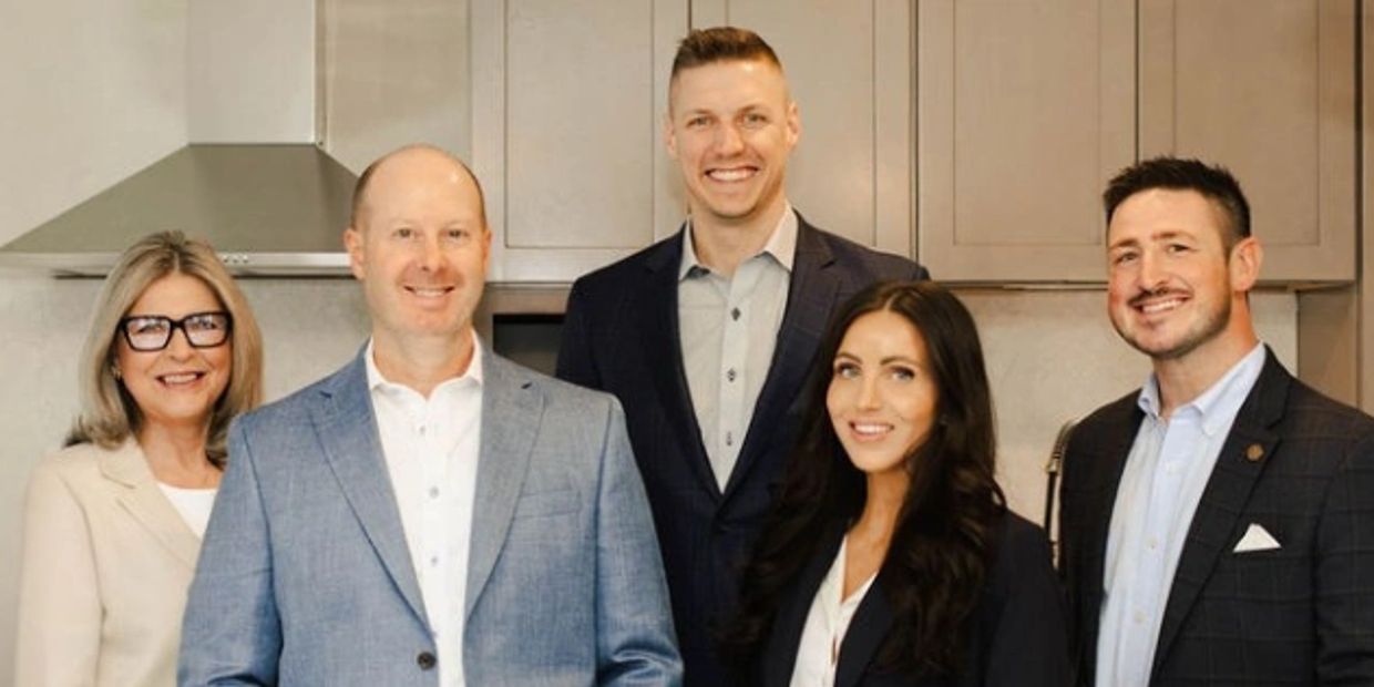 Five professionally dressed people posing in a kitchen.