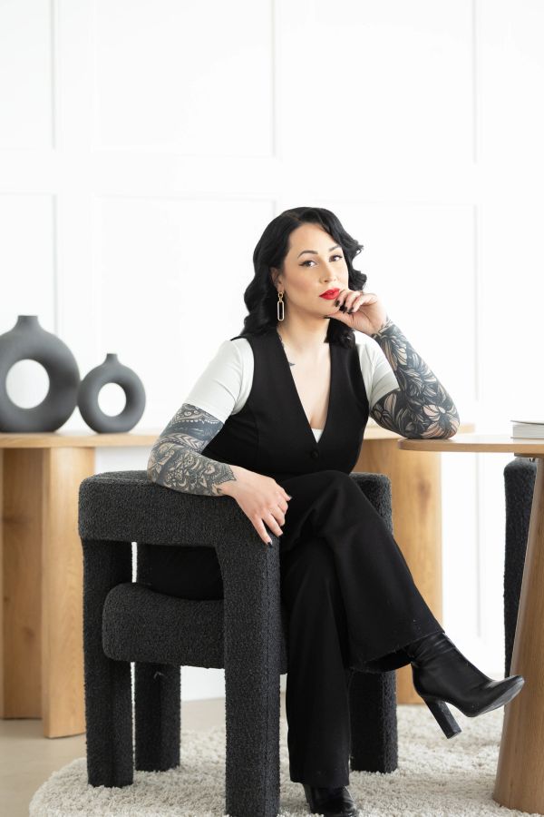 Confident woman with tattoos sitting on a modern black chair.