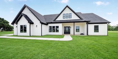Modern white farmhouse with black accents and large green lawn.
