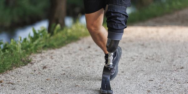 Person with a prosthetic leg walking on a gravel path.
