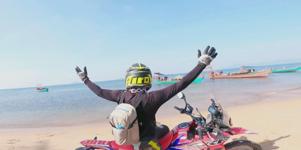 Person on a motorcycle enjoying a beach view with arms raised.