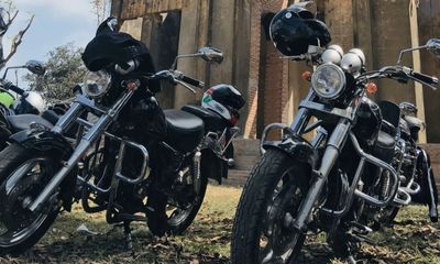 Two black motorcycles parked on grass with helmets resting on them.
