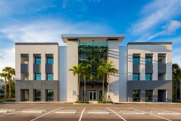 Modern commercial building with palm trees and clear blue sky.