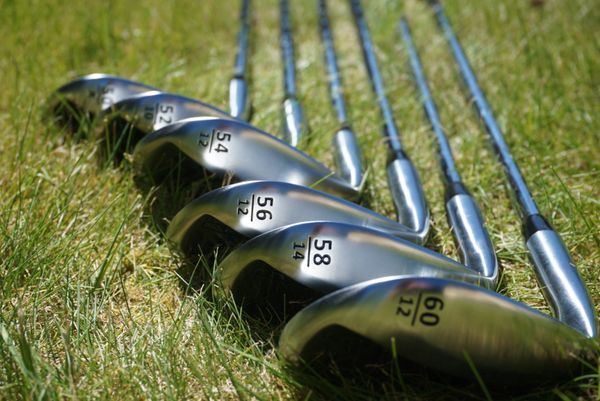 A lineup of golf clubs arranged on grass showing loft angles.