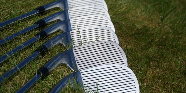 A row of golf clubs lying on the grass with their club faces visible.