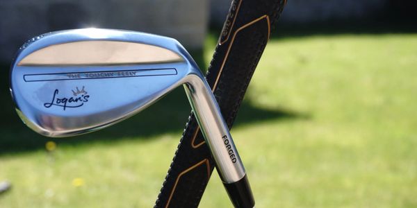 Close-up of a Logan's golf iron with a leather golf bag in the background.