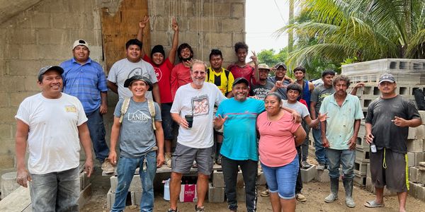 Group of workers posing happily at a construction site with building materials in the background.