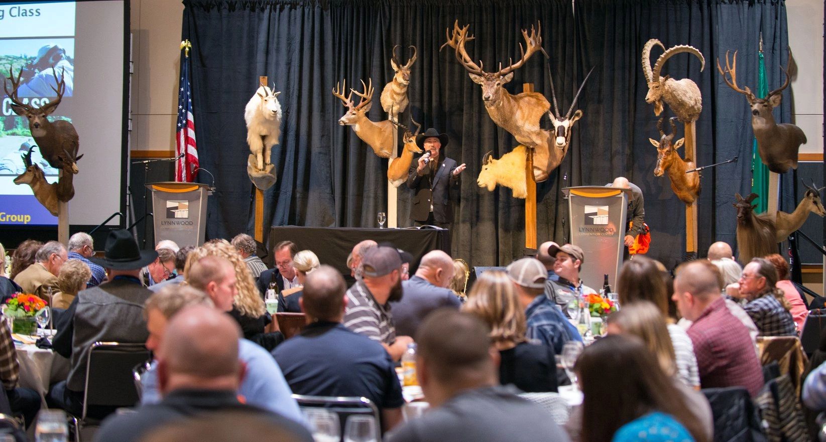 Auction event with mounted animal trophies and audience.