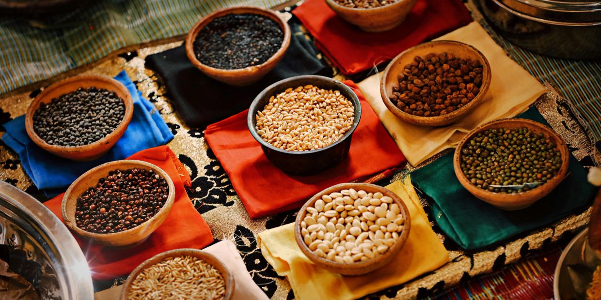 Various grains and seeds in wooden bowls on colorful cloths.