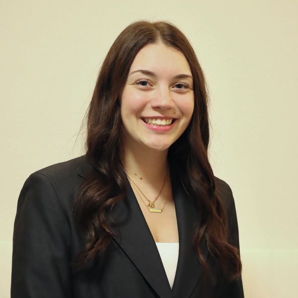 Smiling young woman with long brown hair in a black blazer.