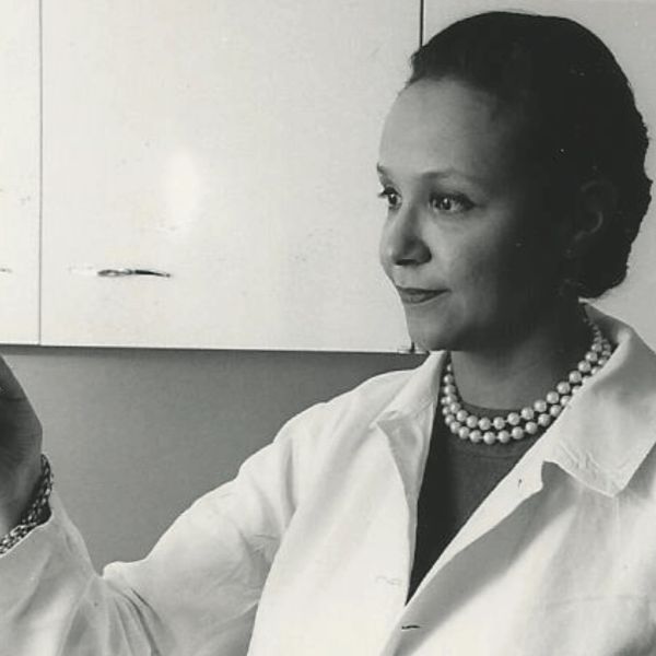 Black and white photo of a woman scientist in a lab coat holding a test tube.