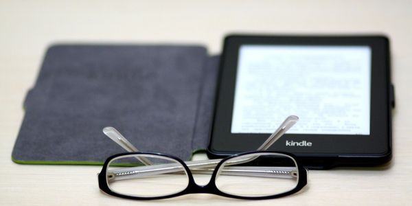 Kindle ebook device and a pair of glasses sat on a table