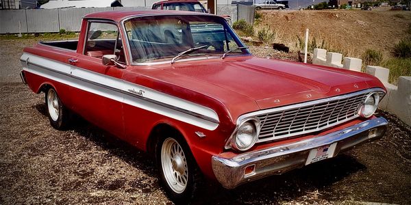 Classic red and white Ford Ranchero pickup truck parked outdoors on a sunny day.