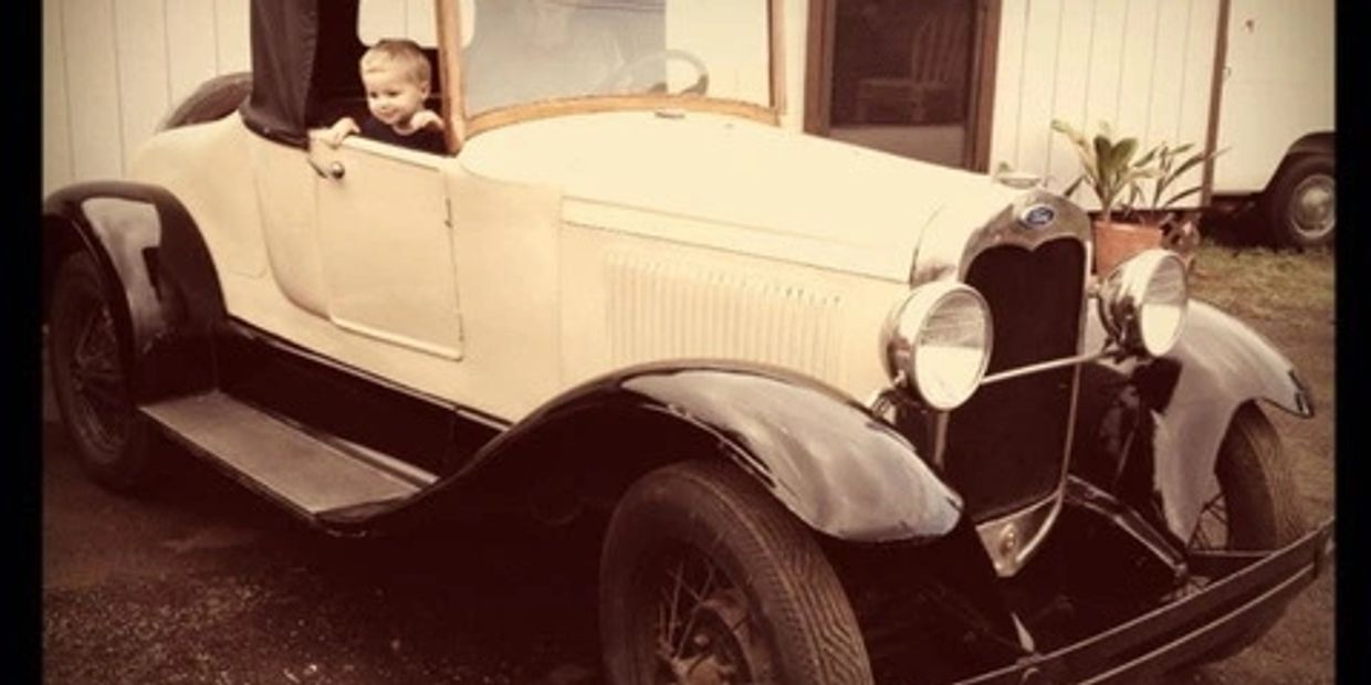 A child sitting in a vintage car with a sepia tone effect.