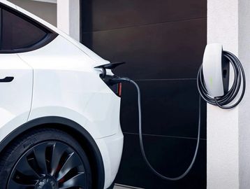 White electric car charging against a black garage door.
