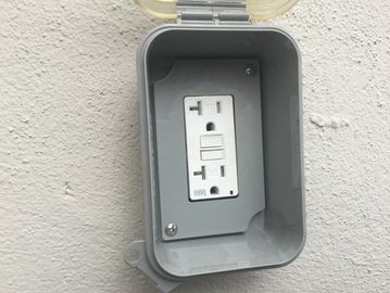 Outdoor electrical outlet with a protective cover mounted on a textured wall.