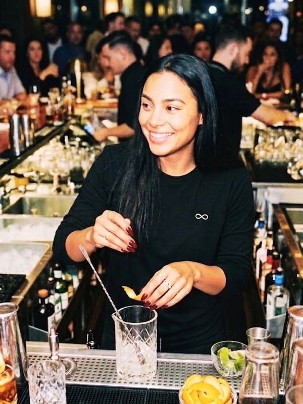 Smiling bartender making a cocktail at a crowded bar.