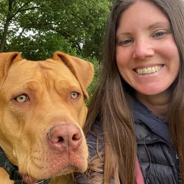 A woman smiling whilst sitting next to a big brown dog.