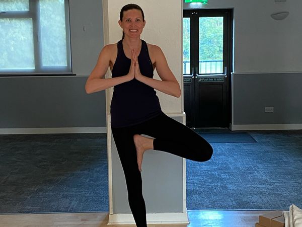 A tall woman practicing yoga, standing in tree pose on a yoga mat.