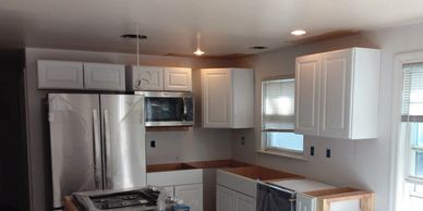 Modern kitchen under renovation with new white cabinets and stainless steel appliances.