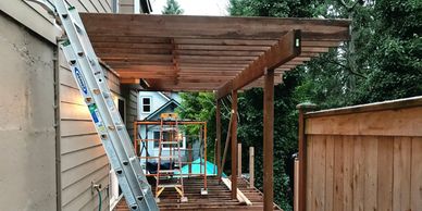 Wooden pergola under construction in a backyard beside a house.